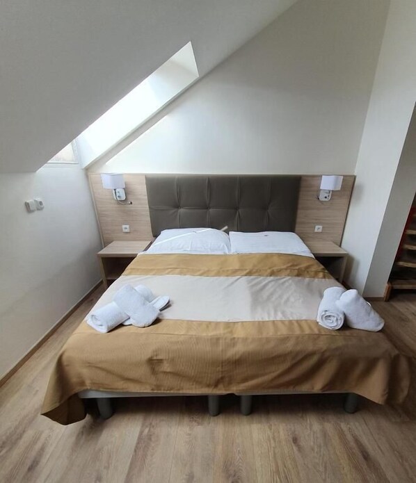 A hotel room with a bed, two bedside tables, a headboard, a skylight, and a wooden floor.