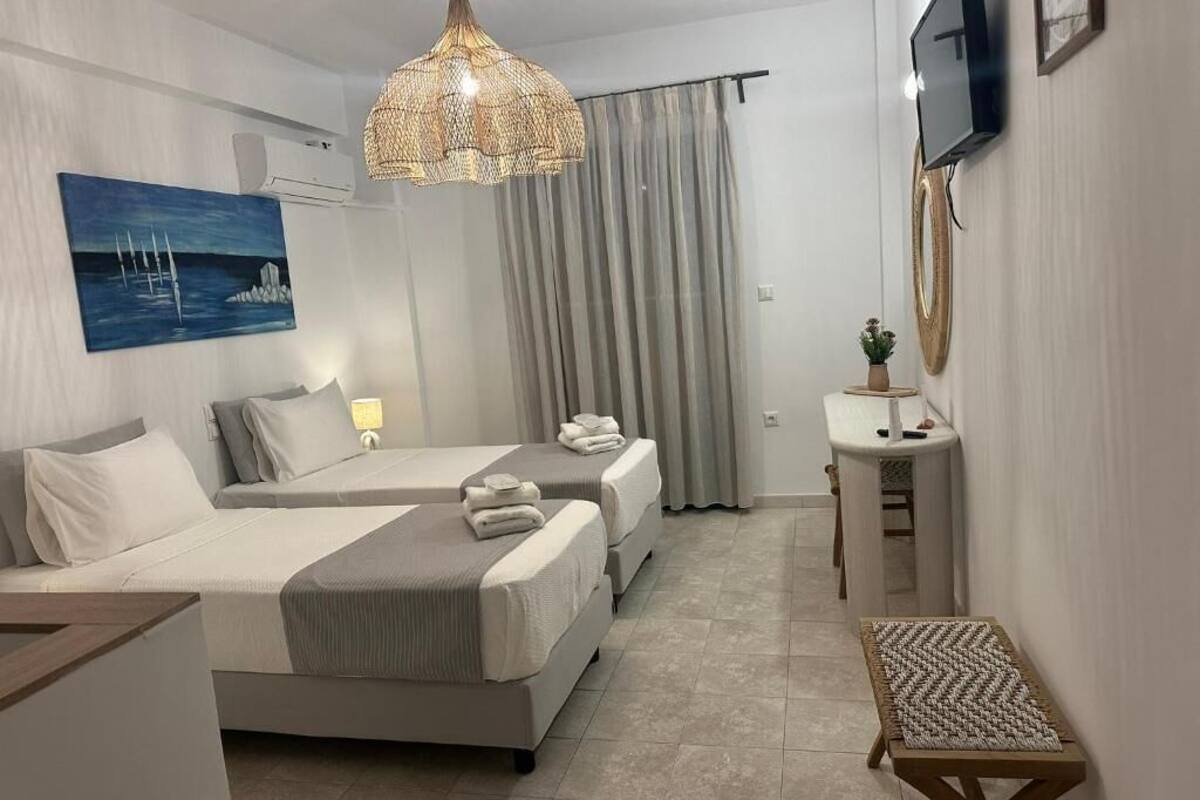 Habitación de hotel con dos camas, televisión, mesita de noche, lámpara colgante y un cuadro en la pared.
