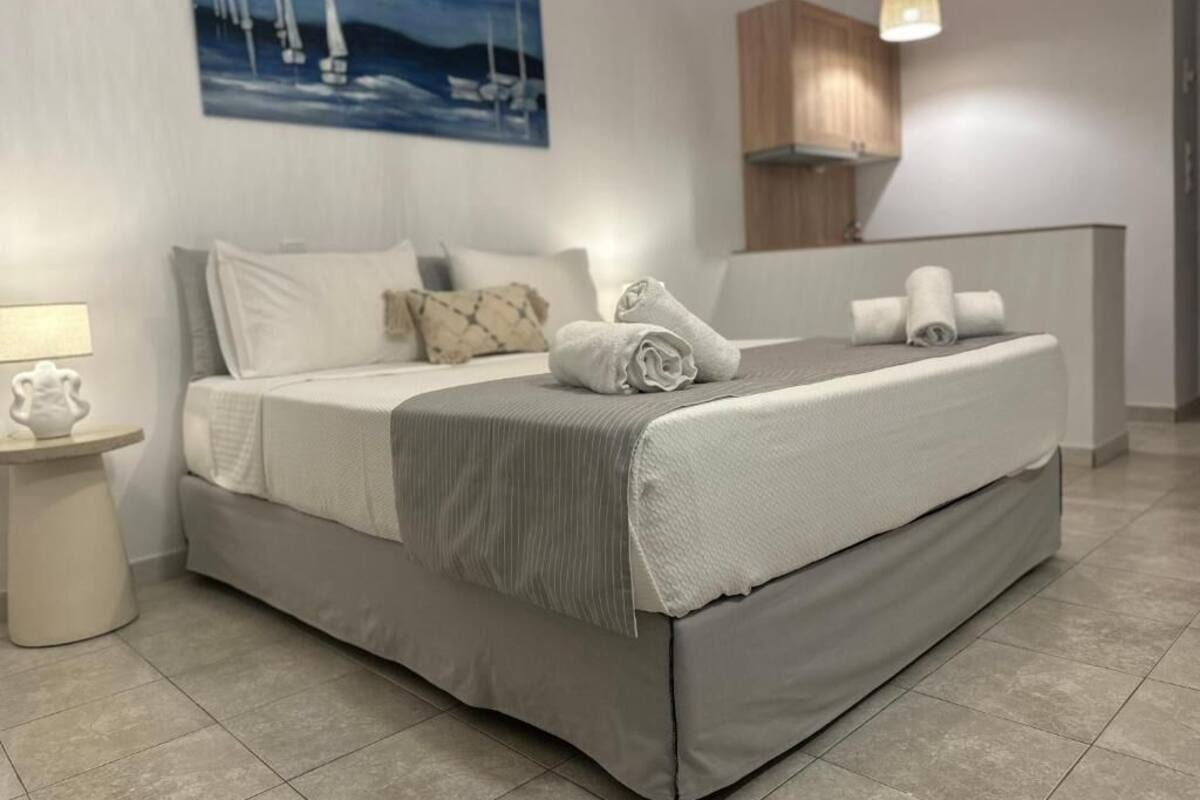 Una cama bien hecha con almohadas y toallas, una mesita de noche con lámpara, y un cuadro de veleros en la pared.