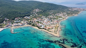 An aerial view of a coastal town with a marina, buildings, and a forested hill in the background. - DEDES APARTMENTS (Agistri)