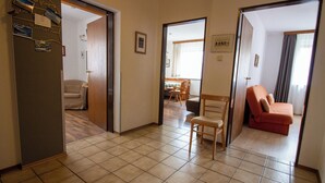 Een hal met een stoel, een bank en een deur naar een kamer met een bed en een tafel.