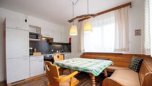 Een compacte keuken met moderne apparatuur, een eettafel met een groen geruit tafelkleed, houten stoelen en een bank met kussens.