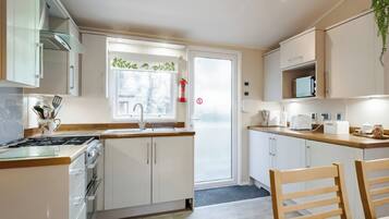 A modern kitchen with white cabinets, a stainless steel stove, a window with a view, and a dining area with a wooden table and chairs.