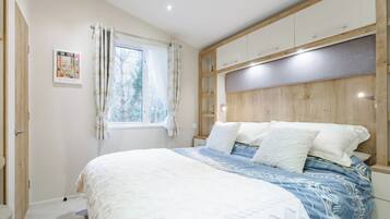 Un dormitorio con cama, ventana con cortinas, cabecero y armarios empotrados.