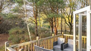 A deck with outdoor furniture, surrounded by trees and a glass door leading to a building.