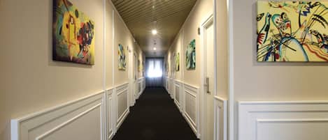 A hallway with white wainscoting, black carpet, and artwork on the walls.
