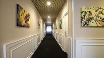 En hall med vit träpanel på väggarna, svart matta och konstverk på väggarna.