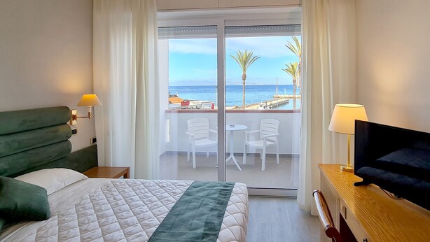 A hotel room with a bed, a TV, a balcony with a view of the sea, and a table with chairs. - Hotel Levante - Isola d'Elba (Cavo)