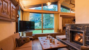 Ein gemütliches Wohnzimmer mit Kamin aus Stein, einem großen Fenster und einem Fernseher.
