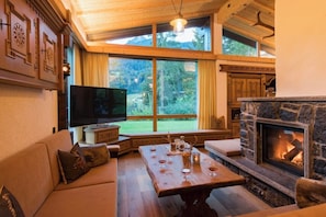 A cozy living room with a stone fireplace, a large window, and a television. - Waldhaus Rappakopf (Tschagguns)
