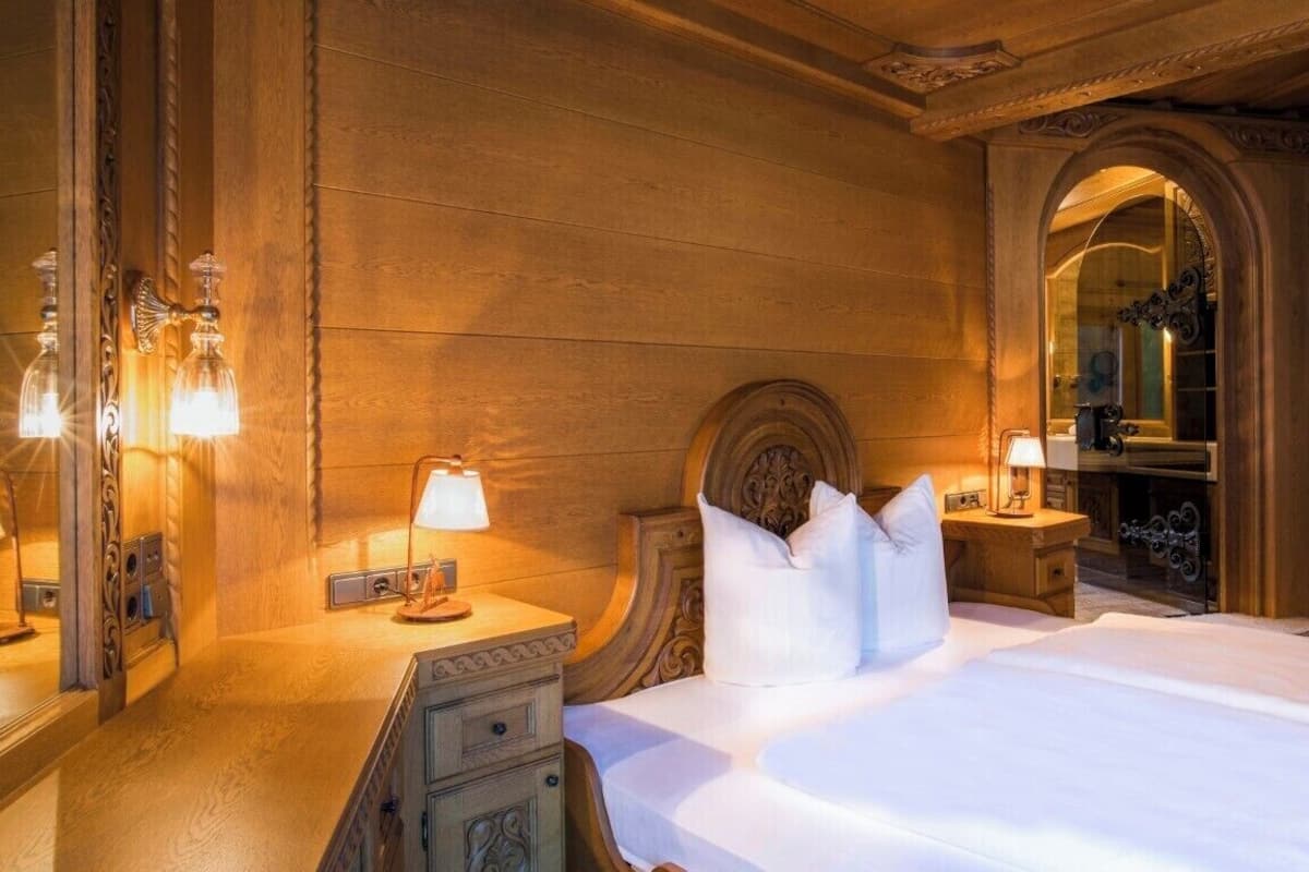 A hotel room with a large bed, wooden paneling, a mirror, and a nightstand with a lamp.