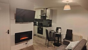 A modern living room with a fireplace, a flat-screen TV, and a dining area with a table and chairs. - kornish holiday cottage (Hayle)
