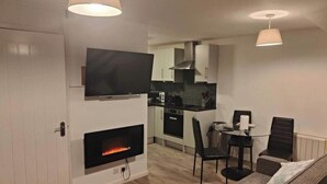 A modern living room with a fireplace, a flat-screen TV, and a dining area with a table and chairs. - kornish holiday cottage (Hayle)
