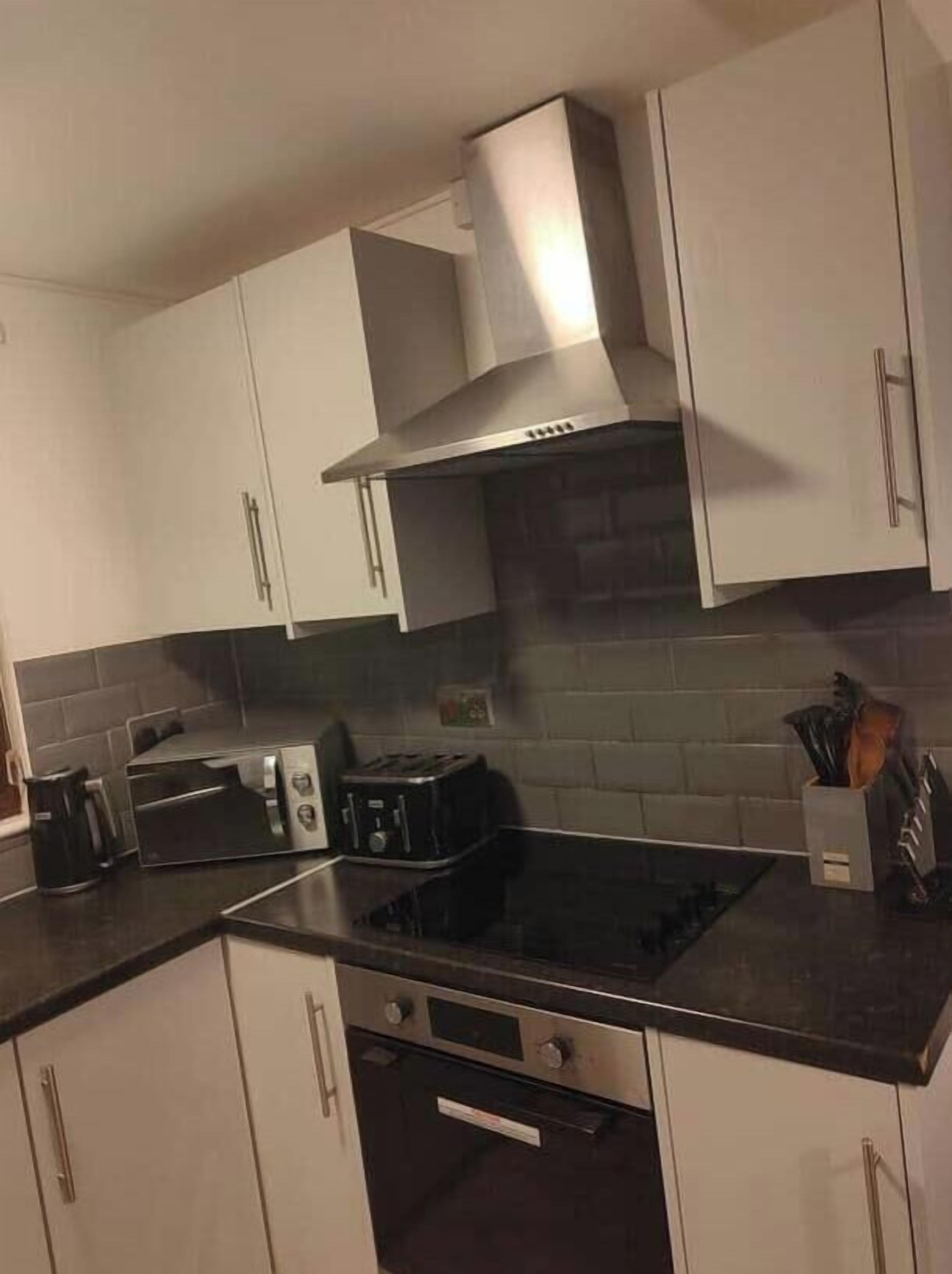 A kitchen with white cabinets, a stainless steel range hood, a toaster, and a coffee maker.