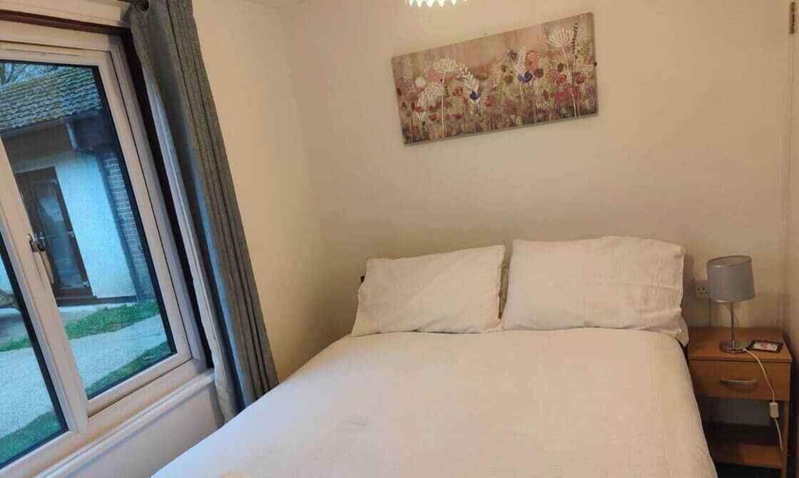 A hotel room with a bed, a window, a painting, and a nightstand.