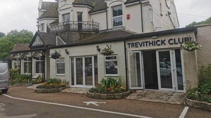 Ein Gebäude mit der Aufschrift 'TREVITHICK CLUB', einem Balkon und Blumenbeeten im Vordergrund.