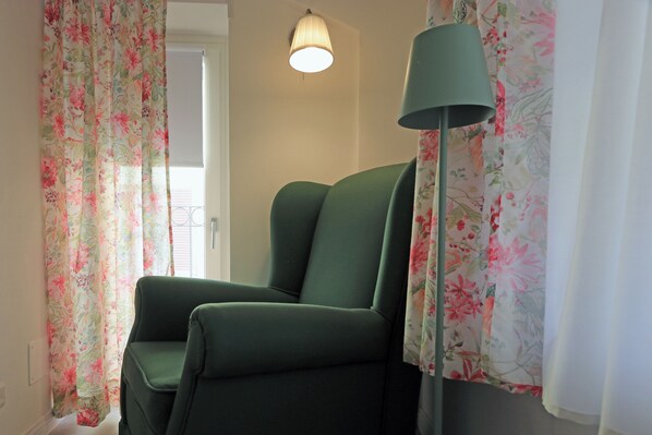 A room with a green chair, floral curtains, a lamp, and a door. - Lùlù Guest House (Dernice)