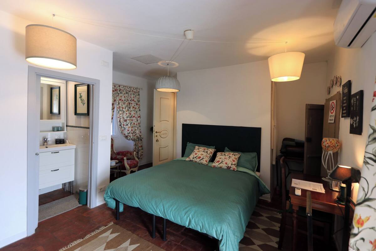 Un dormitorio con cama, mesitas de noche, escritorio, silla, espejo, puerta y equipo de aire acondicionado.