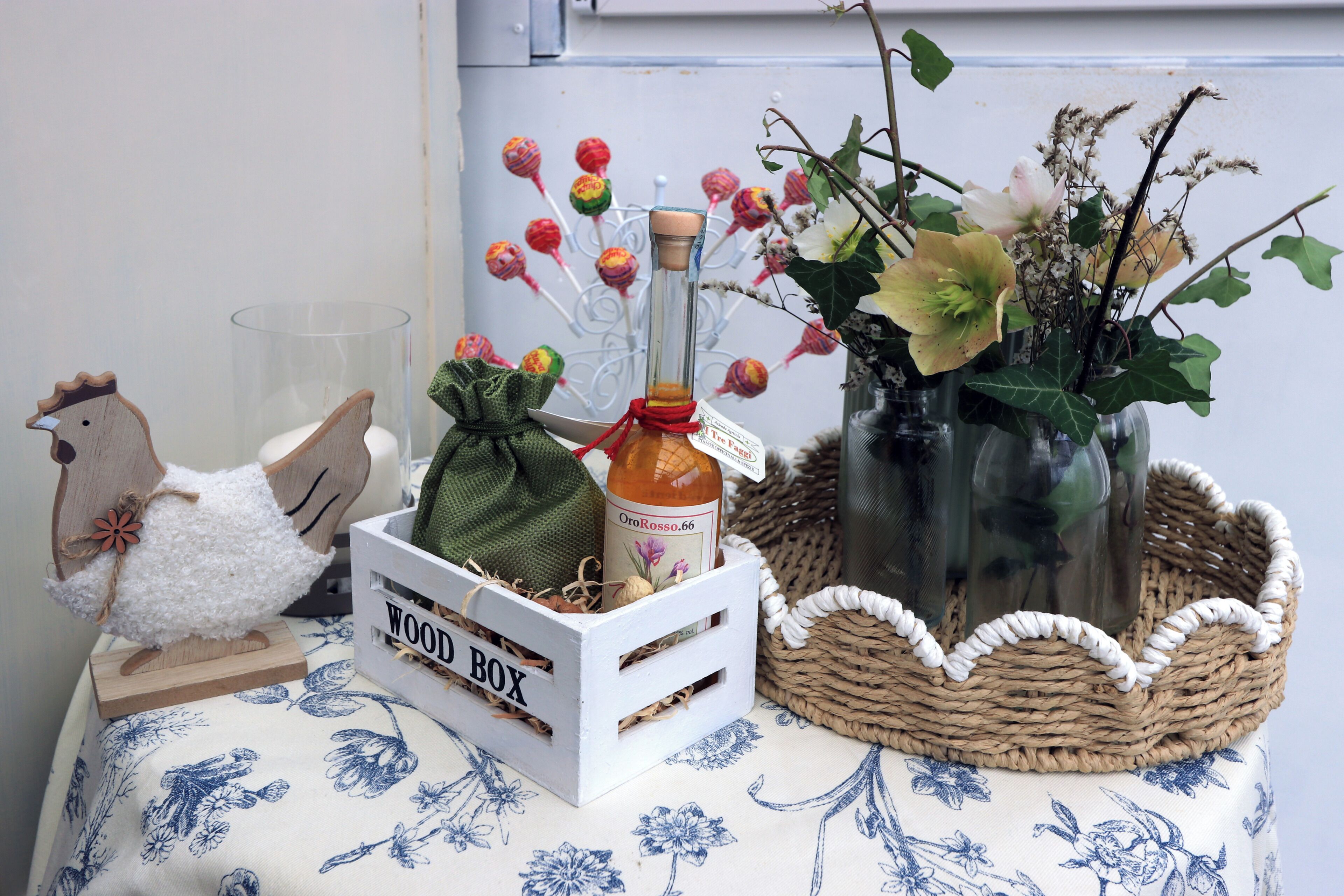 A wooden box labeled 'WOOD BOX' with a bottle and a decorative item on a table with a floral tablecloth.