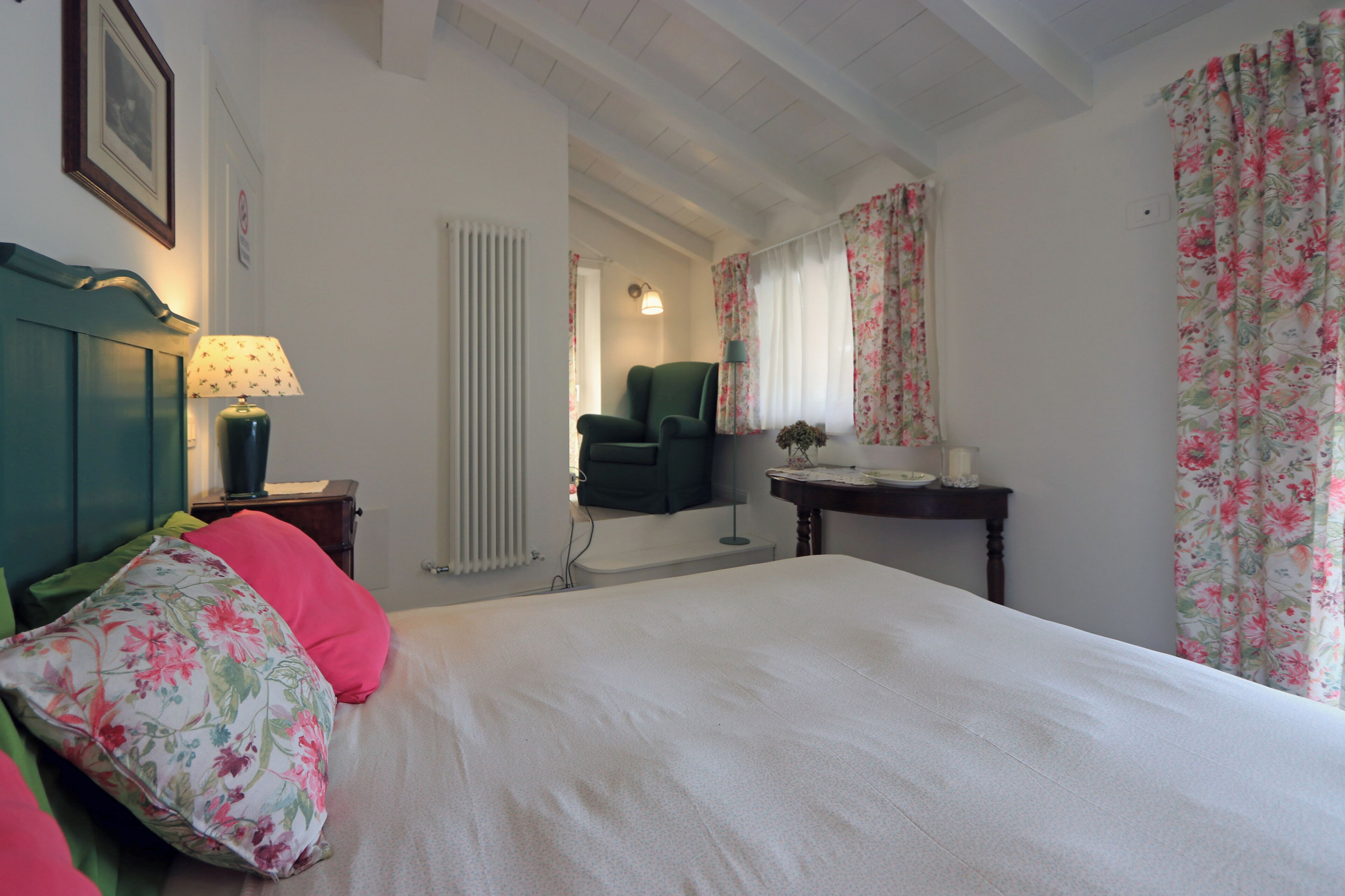 A bedroom with a bed, a chair, a table, and a radiator.