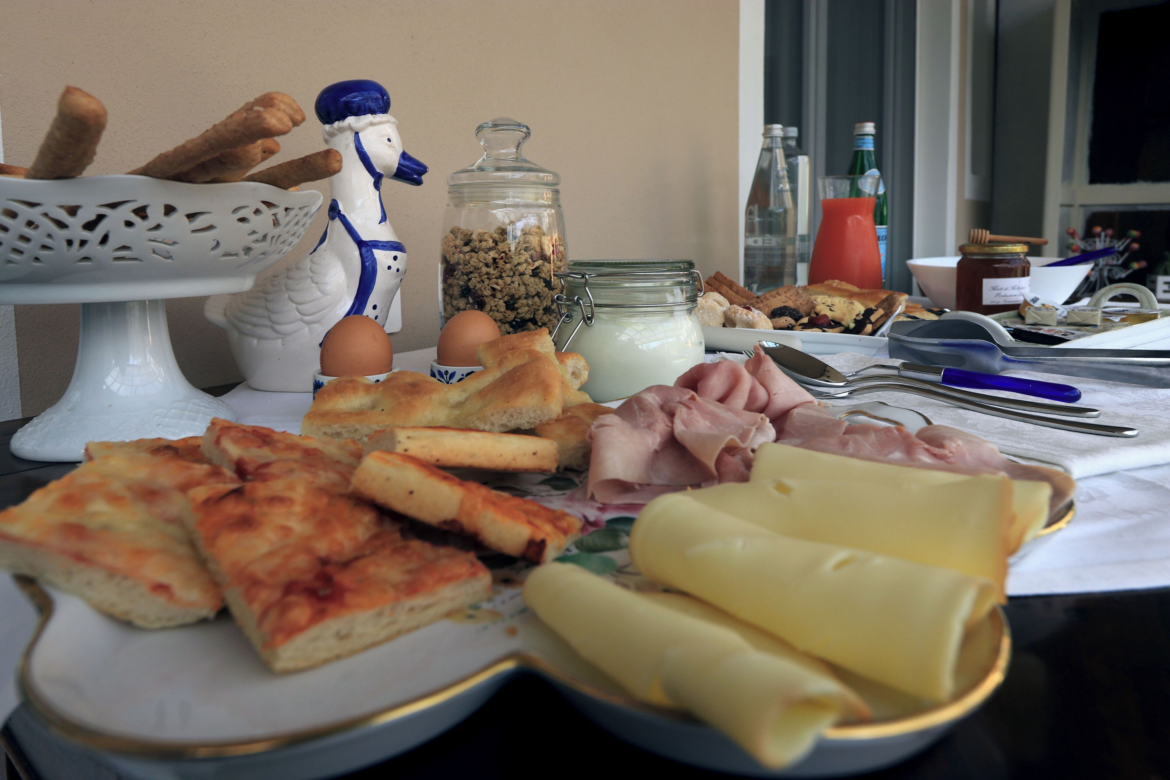 Ein Esstisch mit verschiedenen Speisen, darunter Brot, Käse, Eier und eine dekorative Keramikfigur.