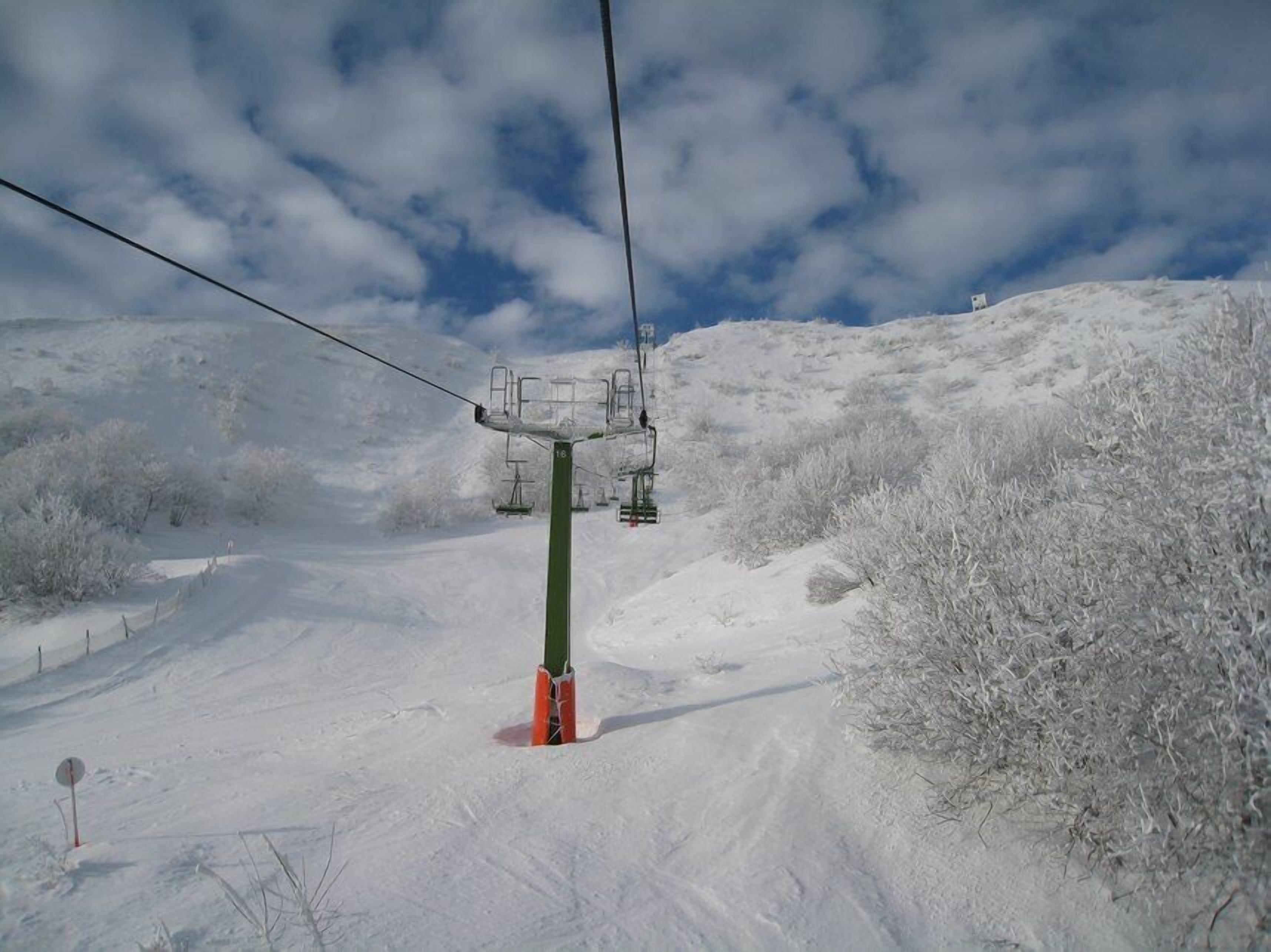 Un télésiège suspendu à un câble, un poteau vert agrémenté de touches de rouge, et un paysage enneigé à la végétation clairsemée.