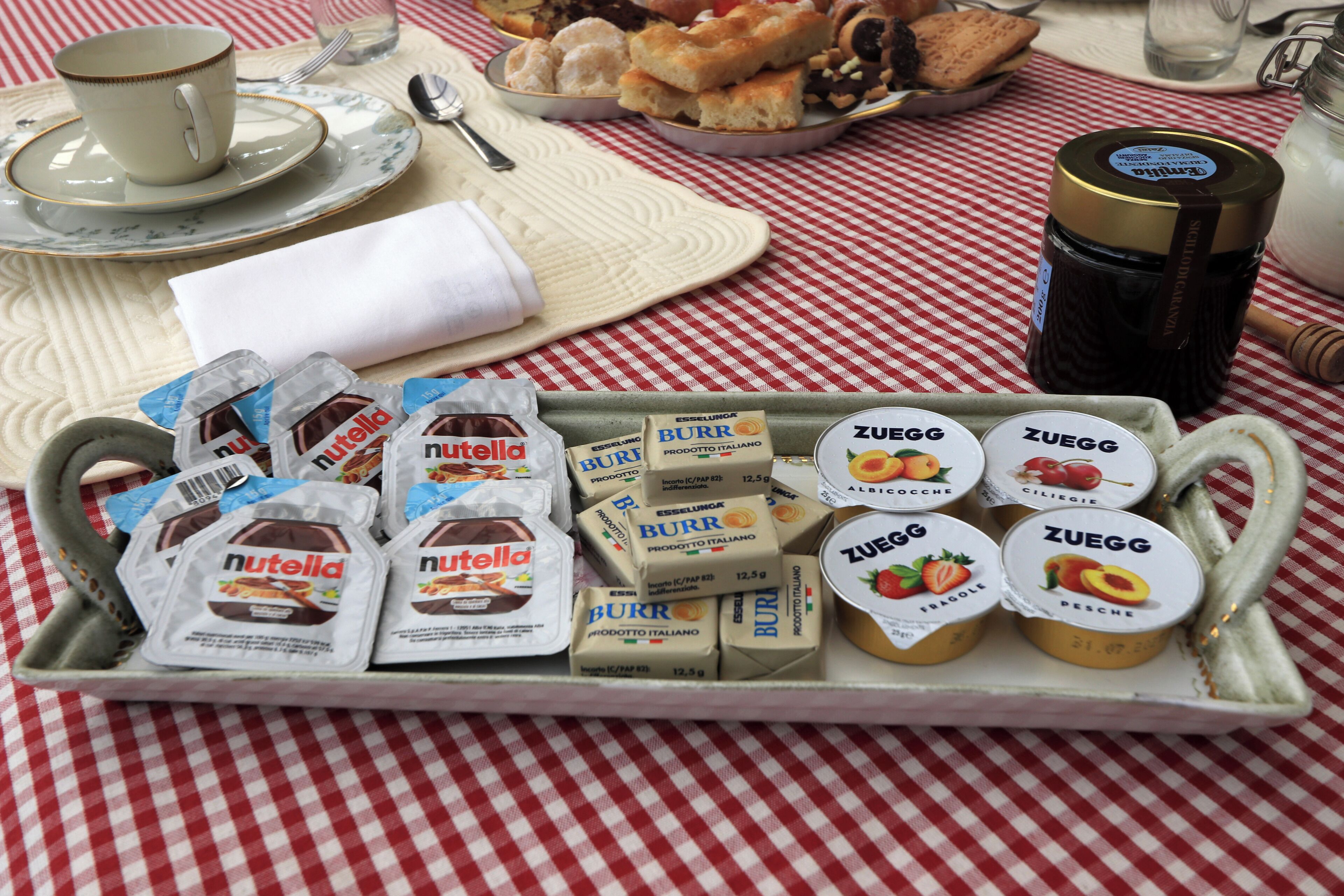 Une assiette contenant divers aliments, notamment du Nutella, des burritos et un yaourt Zuegg, posée sur une nappe à carreaux.