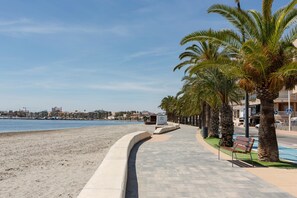 Eine Uferpromenade mit gewundener Uferpromenade, Palmen und Blick auf das Meer sowie entfernte Gebäude.