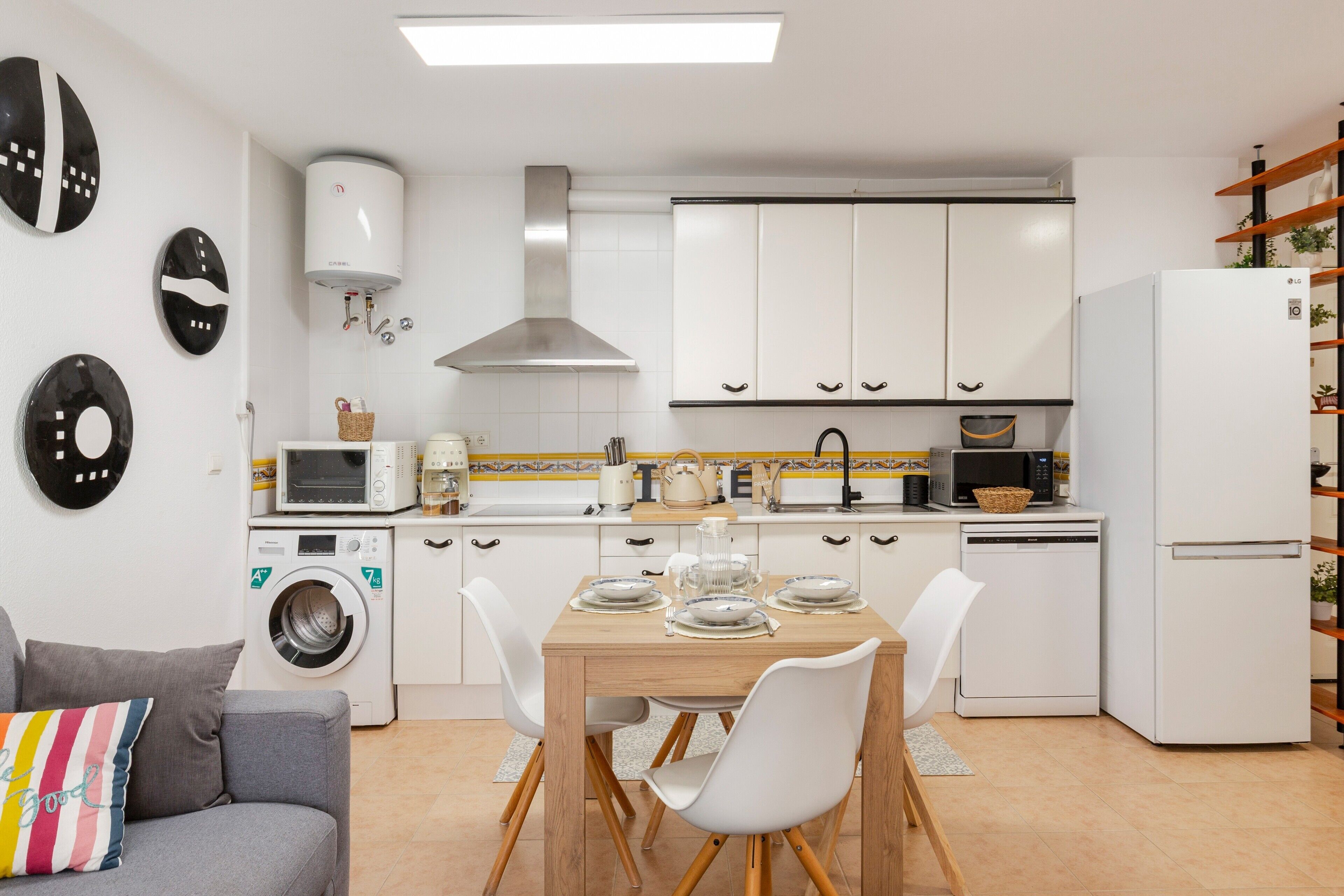 Een compacte keuken met witte kastjes, een magnetron, een wasmachine en een eethoek met een tafel en stoelen.