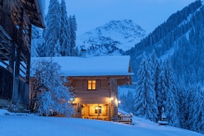A wooden cabin with a snow-covered roof, surrounded by snow-laden trees and mountains. - Berghaus Manuaf (Tschagguns)