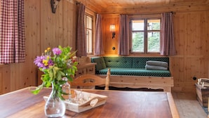 En stuga med träpanel på insidan, en grön soffa, rutiga gardiner, ett hjorthuvud som hänger på väggen och ett fönster med utsikt över grönskan.
