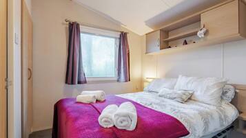 A bedroom with a bed, a window with curtains, a shelf with a decorative item, and a towel on the bed.