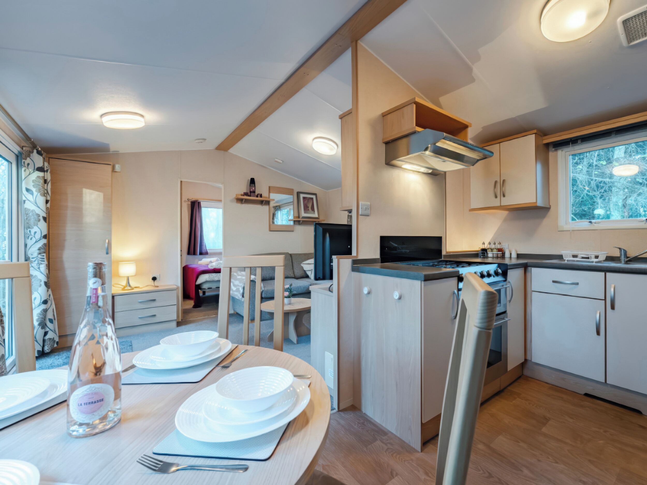A compact kitchen with modern appliances, a dining area with a table set for two, and a cozy bedroom visible through an open door.
