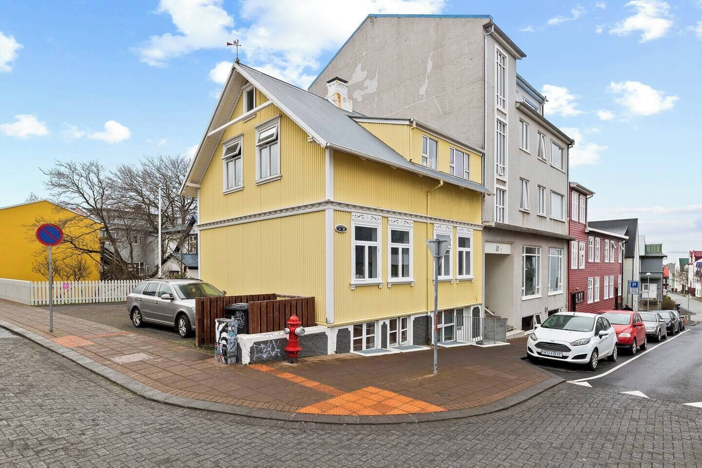 Un bâtiment jaune avec un toit gris, une clôture blanche et un potelet d’hydrant rouge.