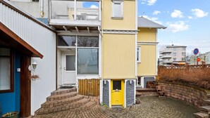 Een woongebouw met twee verdiepingen, met een gele voordeur, een zichtbare trap naar de ingang en een geplaveid binnenterrein.