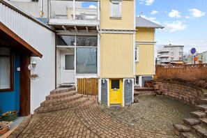 A two-story residential building with a yellow front door, a visible staircase leading to the entrance, and a paved courtyard. - The Heart of Downtown Reykjavík (Reykjavík)