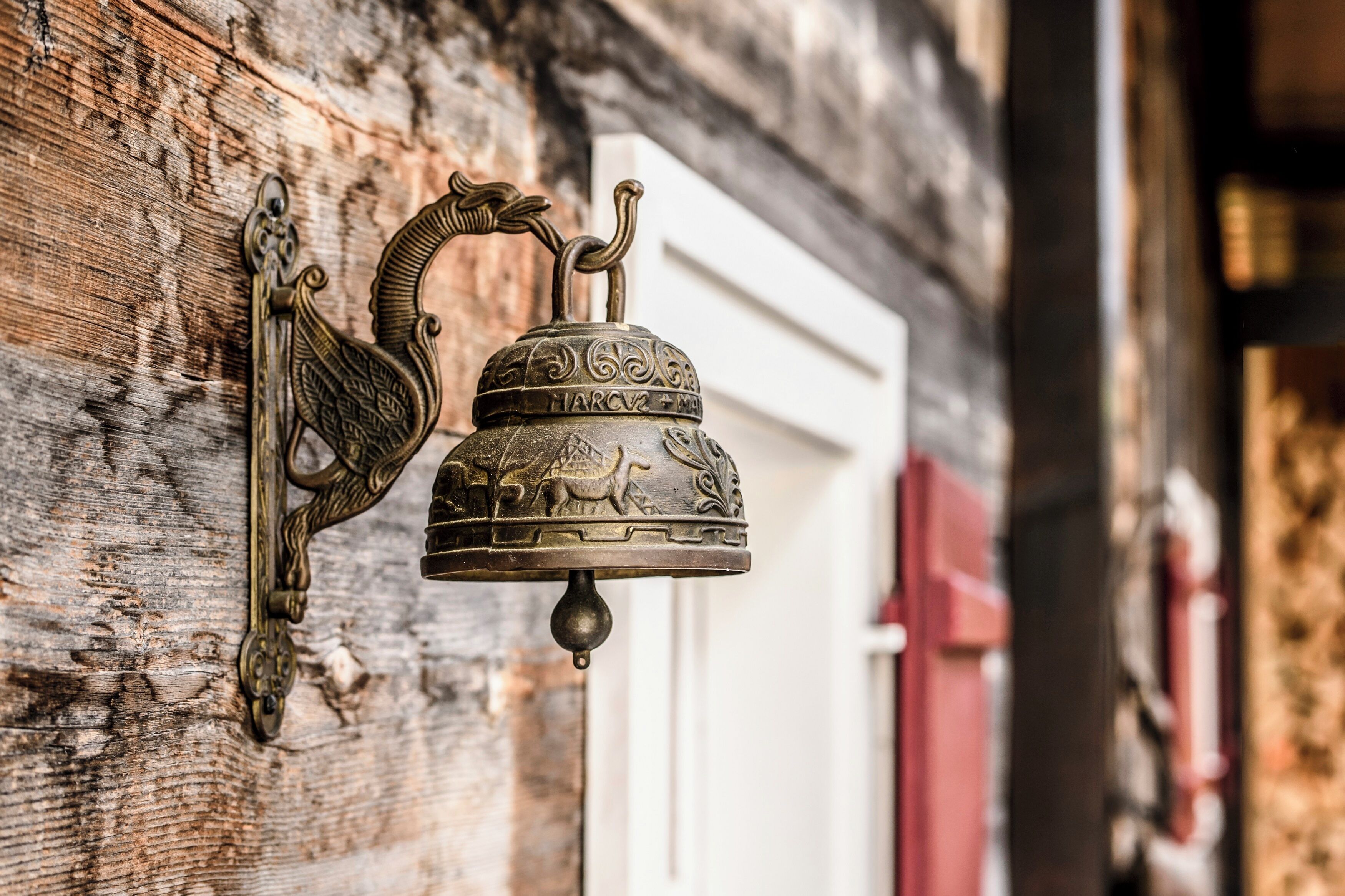A wall-mounted bell with a decorative design, mounted on a wooden surface.