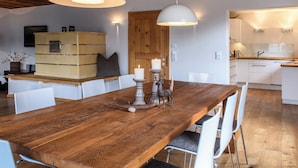 Ein Holztisch mit weißen Stühlen, eine Holzkommode und eine Holzbalkendecke.