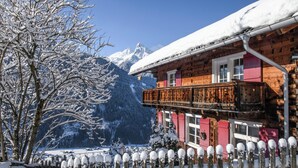 Eine Holzhütte mit Balkon, umgeben von schneebedeckten Bäumen und Bergen.