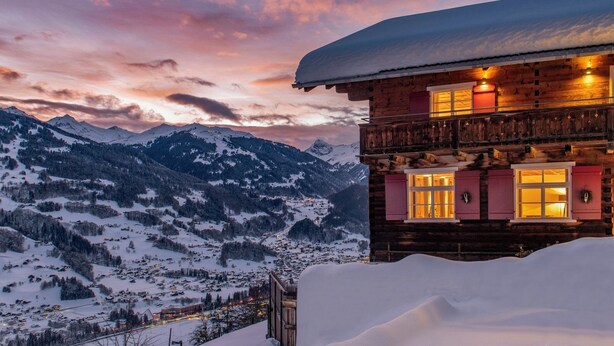 Eine Holzchalet mit einem mit Schnee bedeckten Dach, Fenstern mit Fensterläden und einem Balkon.