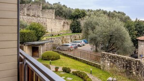 A courtyard with stone walls, parked cars, and a view of a historic stone building. - Lemon House 3 by Wonderful Italy (Gardone Riviera)