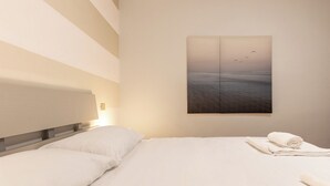 A hotel room with a bed, a headboard, a wall-mounted painting, and a rolled towel on the bed. - Lemon House 3 by Wonderful Italy (Gardone Riviera)