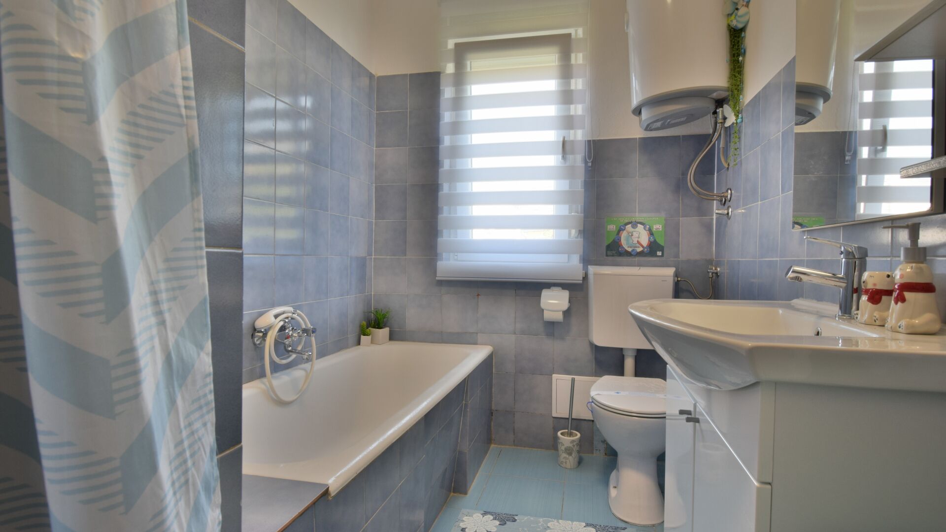 Un bagno con vasca, servizi igienici e lavabo, con piastrelle blu e una finestra.