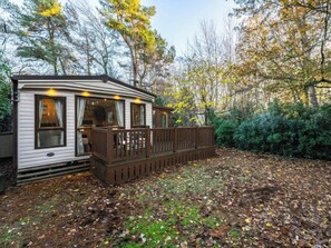 Une maison mobile dotée d’une terrasse, entourée d’arbres et d’un sol recouvert de feuilles.