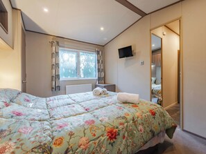 Une chambre à coucher avec un lit, une fenêtre avec des rideaux, un radiateur, un téléviseur fixé au mur et une porte donnant sur une autre pièce.