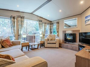 A modern living room with a sofa, armchairs, a coffee table, a TV, and a fireplace. - The But n Ben - Kelling Heath Holiday Park (Holt)