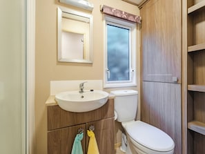 A bathroom with a sink, mirror, toilet, and wooden cabinets. - The But n Ben - Kelling Heath Holiday Park (Holt)