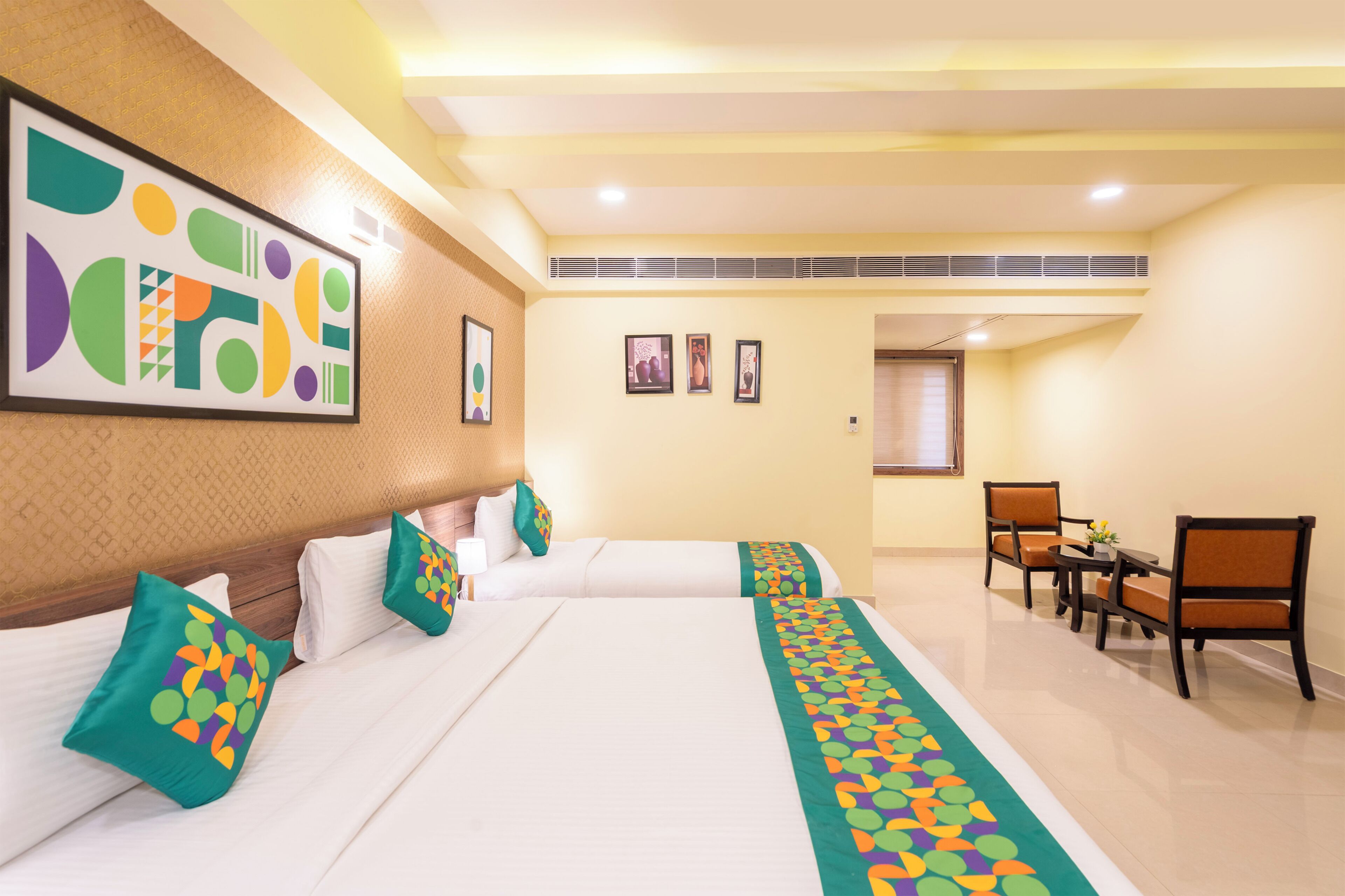 A hotel room with two beds, a desk with chairs, and a large abstract painting on the wall.