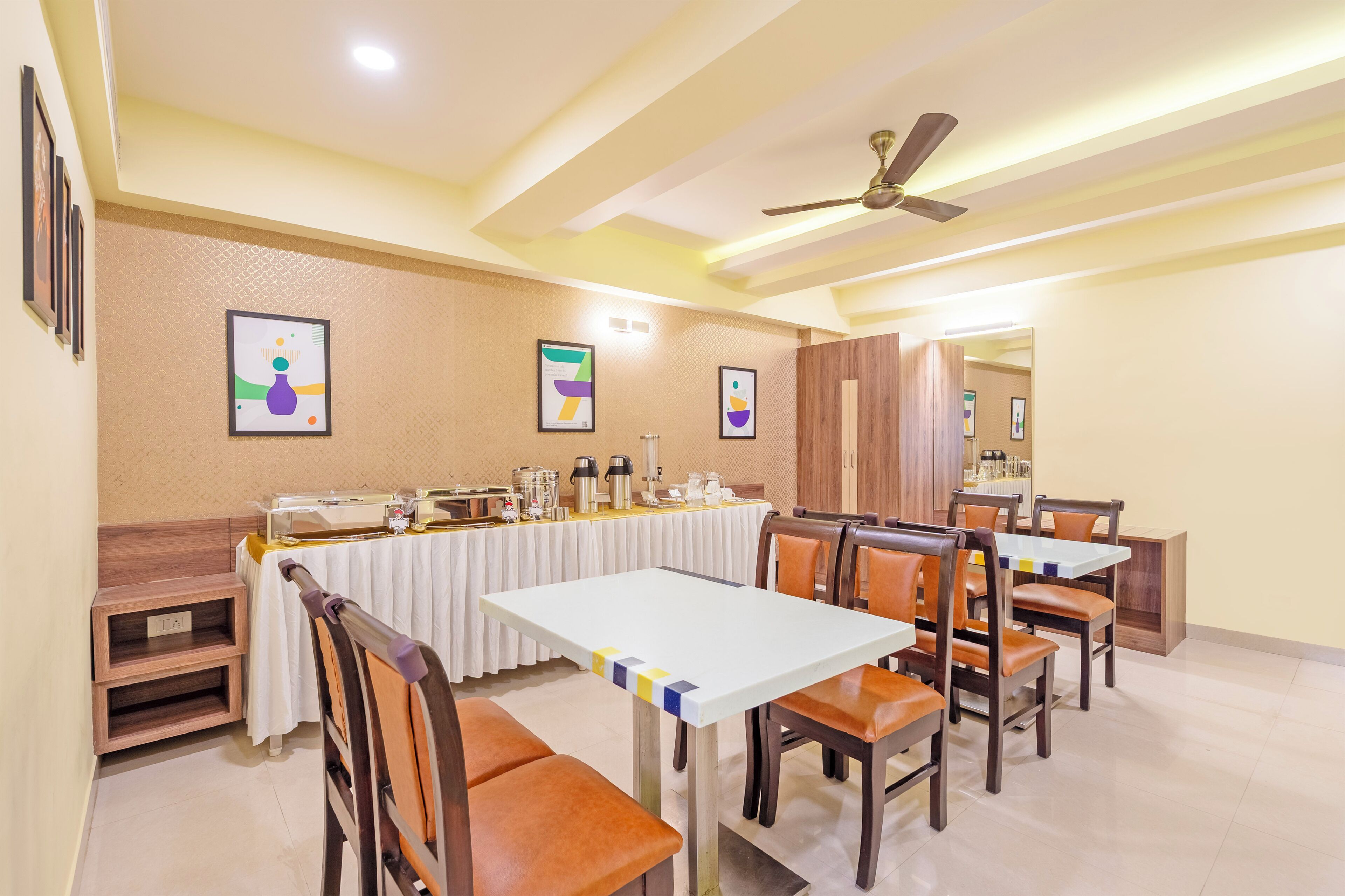 A dining area with a long table, chairs, a ceiling fan, and framed artwork on the walls.
