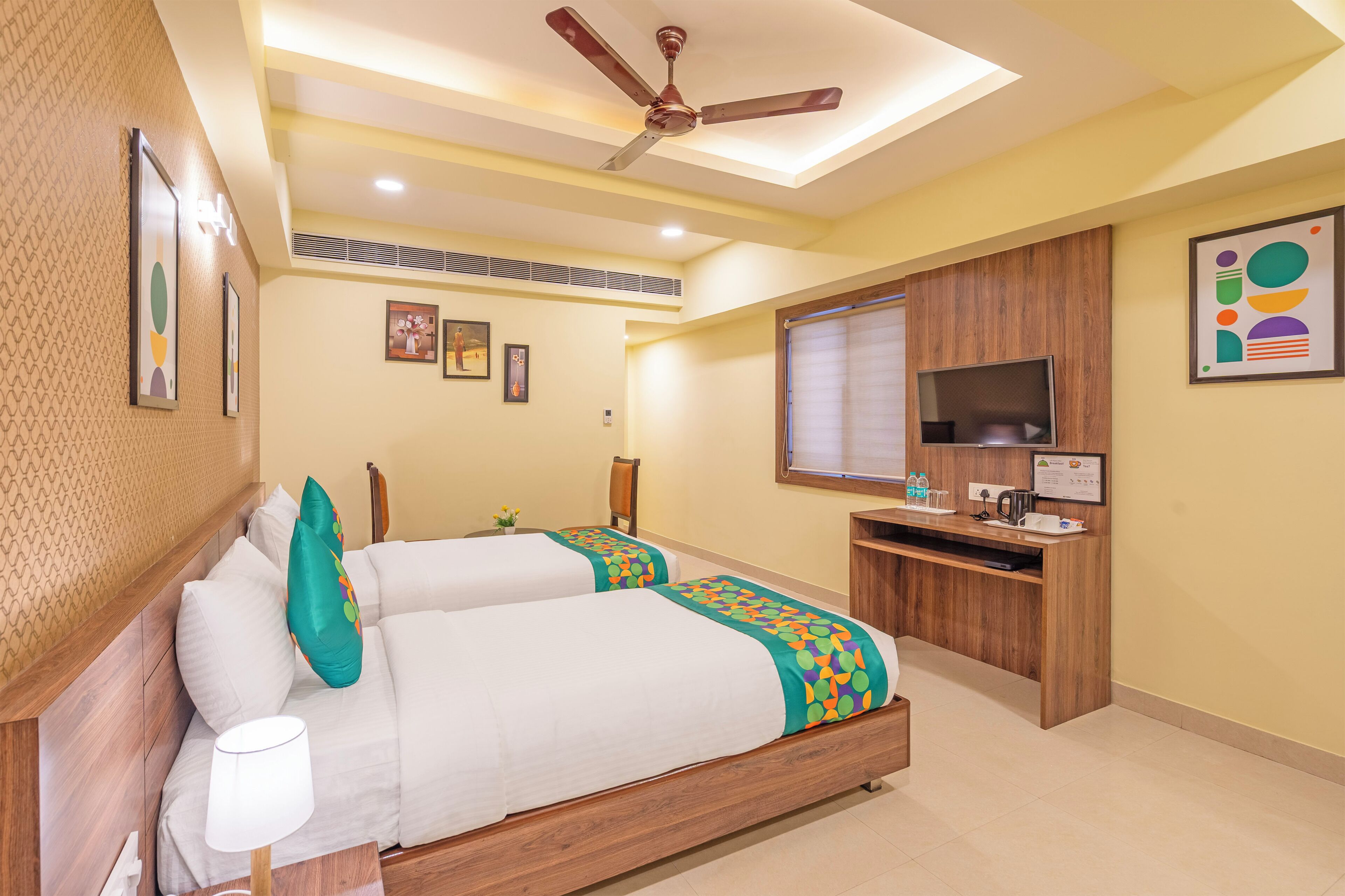 A hotel room with two beds, a desk, a TV, and a ceiling fan.